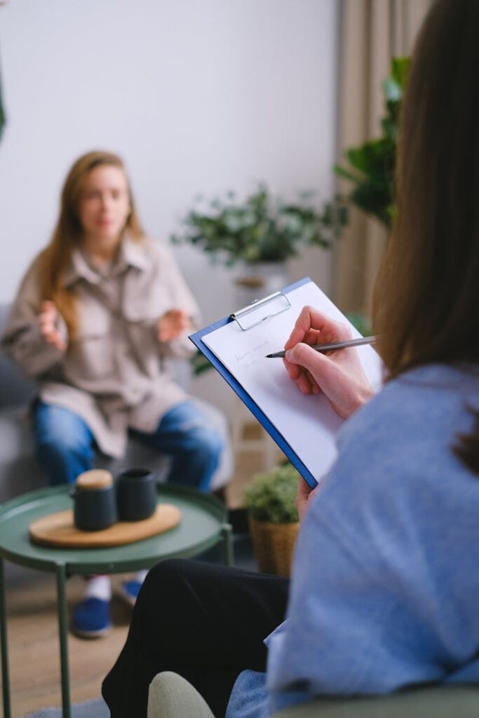 pexels-photo-7176036 Unrecognizable female psychologist taking notes on clipboard while listening to patient sitting on blurred background during psychotherapy consultation in office